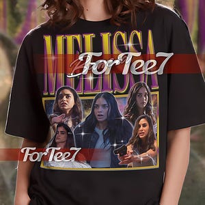 May include: Black unisex t-shirt with a graphic print of a group of women with the text "Melissa For Tee7" in yellow and purple. The graphic is set against a dark blue background with stars and lightning bolts.