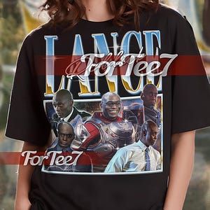May include: Black unisex t-shirt with a graphic print of a group of people in a space scene. The text "Lance ForTee7" is printed on the shirt in a blue and white font.