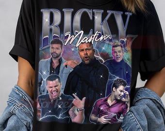 May include: Black unisex t-shirt featuring a graphic of Ricky Martin with the text "RICKY Martin" in a silver and blue design. The shirt has a crew neck and short sleeves. The words "UNISEX SHIRT" are at the top.
