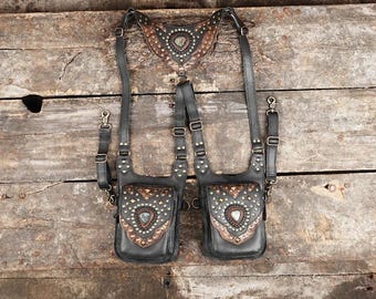 May include: Two black leather pouches with intricate brown and silver designs and gemstone accents. The pouches are attached to a black leather harness with straps.