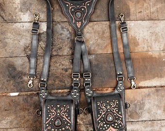 May include: A black leather double holster with intricate designs and turquoise accents. The holster has two pockets and is attached to a harness with adjustable straps.