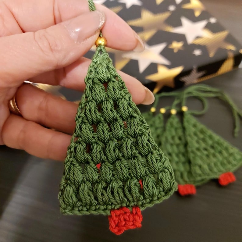 May include: A set of four green crocheted Christmas tree ornaments with red felt bases and gold beads at the top.