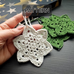 Puede incluir: Un adorno de estrella tejido a crochet blanco con un adorno de estrella tejido a crochet verde en el fondo. La imagen incluye la palabra "PATTERN" en la parte superior central de la imagen.