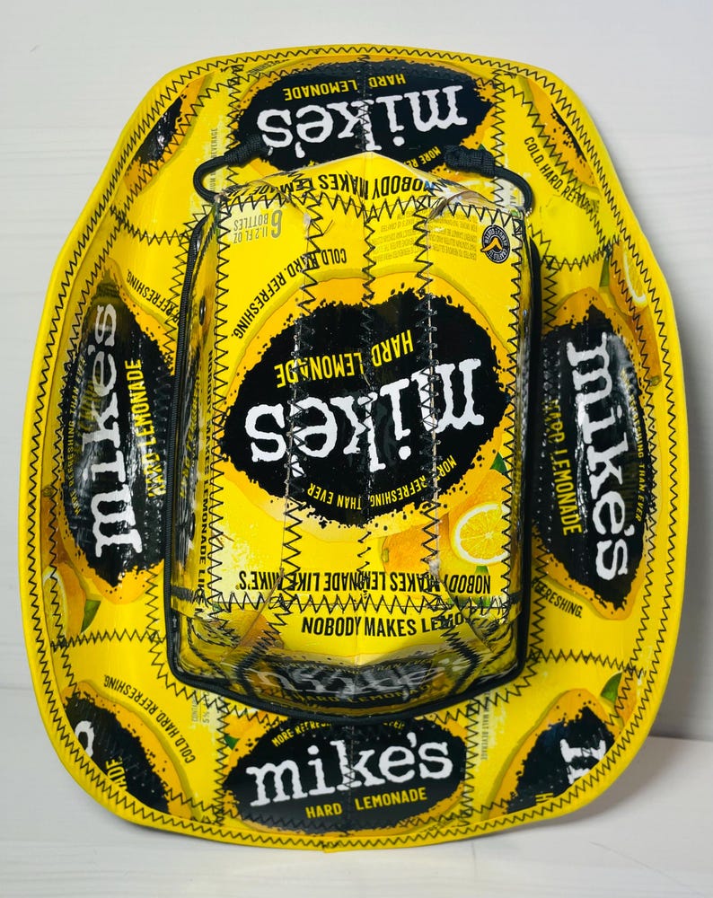 Puede incluir: Un sombrero de vaquero amarillo y negro con el tema de Mike's Hard Lemonade. El sombrero est&aacute; hecho de las latas de la bebida y presenta el logotipo y el texto de la marca. Un art&iacute;culo &uacute;nico y hecho a mano.
