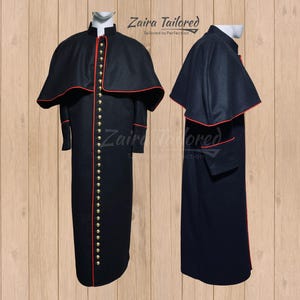 Może przedstawiać: Czarna sutanna duchowna z czerwonym obszyciem i złotymi guzikami. Sutanna ma pelerynę przymocowaną do ramion. Tekst "Zaira Tailored, Tailored to Perfection" jest widoczny na zdjęciu.