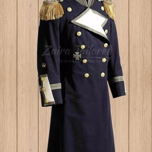 Puede incluir: Un abrigo azul oscuro de doble botonadura con botones y ribetes dorados. El abrigo tiene un cuello y puños blancos con detalles dorados. El abrigo es de estilo tradicional con una longitud larga y un cuello alto.
