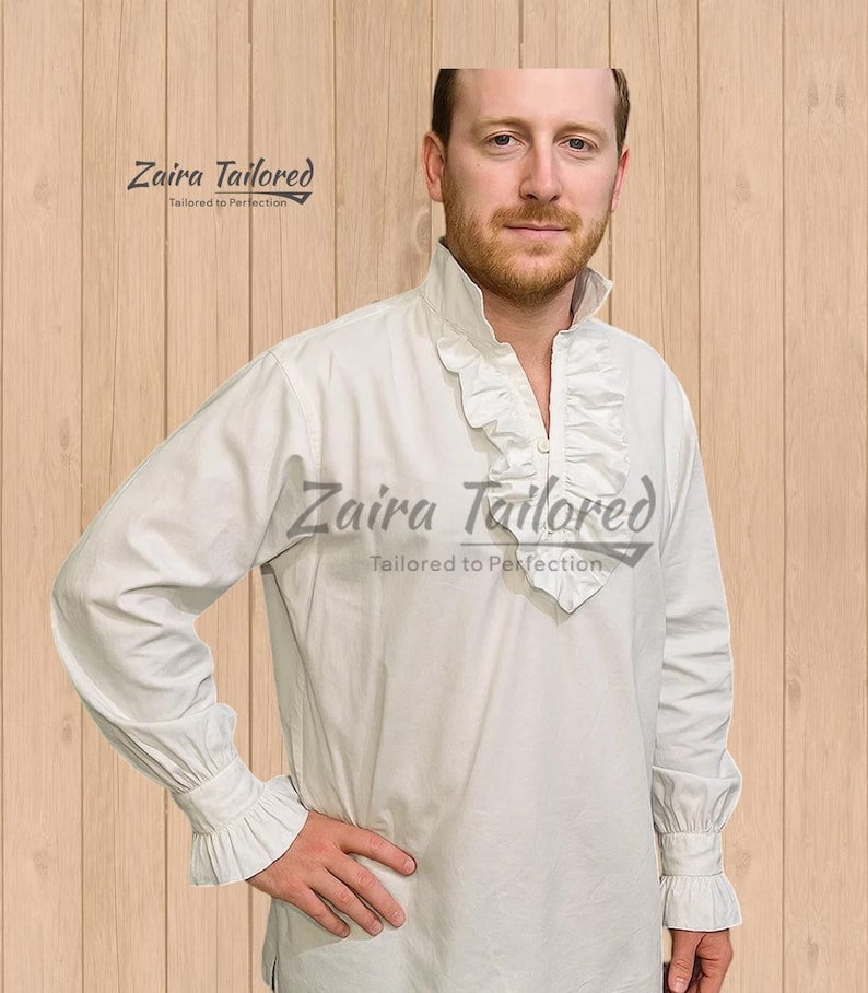 Op de afbeelding: Een wit overhemd met lange mouwen en een kraag en manchetten met ruches. Het overhemd heeft een knoopsluiting aan de voorkant en is gemaakt van een zachte, soepele stof. De tekst "Zaira Tailored" is op het overhemd gedrukt. Het is een historisch of theatraal kledingstuk.
