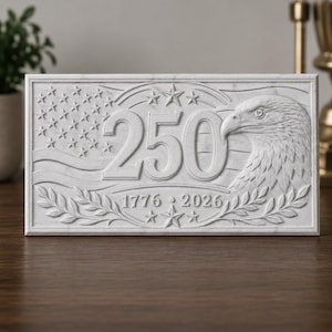 May include: A rectangular white stone plaque featuring a relief carving of a bald eagle, the number 250, and the years 1776 and 2026. The design includes a stylized American flag with stars and stripes, framed by laurel leaf branches and stars.