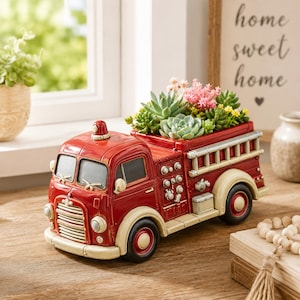 May include: A red and cream-colored fire truck planter filled with succulents and small flowers. The vintage-style truck has a ladder, headlights, and a siren. The planter sits on a wooden surface near a window.