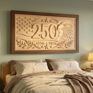 A wooden framed wall art piece with a carved design. The artwork features the number "250" with an eagle, stars, and the years "1776-2026". The frame is brown, and the carved design is a lighter wood color.