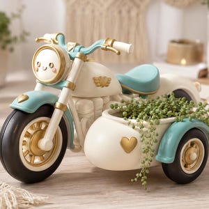 Könnte beinhalten: Dekorativer Motorrad-Blumentopf in Creme, Gold und Türkis. Das Motorrad hat einen Beiwagen, der mit Grünzeug gefüllt ist. Das Motorrad hat ein lächelndes Gesicht auf dem Scheinwerfer. Die Räder sind schwarz mit goldenen Akzenten.