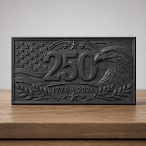 May include: A rectangular black plaque featuring a relief design of a bald eagle, the number 250, and the years 1776 and 2026. The design includes a stylized American flag with stars and stripes, framed by laurel branches and additional stars.