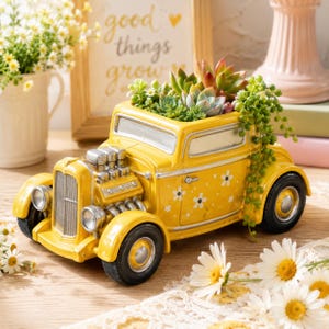 Puede incluir: Una jardinera amarilla con forma de coche antiguo llena de suculentas. La jardinera tiene detalles de margaritas blancas y detalles cromados del motor. Las ruedas del coche son negras y el diseño general es caprichoso y decorativo.