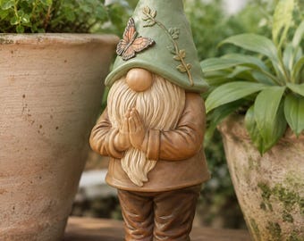 May include: A garden gnome figurine with a sage green pointed hat featuring a butterfly and vine detail. The gnome has a long cream-colored beard, wears a brown tunic and pants, and stands barefoot on a small green base decorated with colorful flowers.