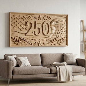 A large, rectangular wooden wall art piece with a carved design. The design includes the number "250", an eagle, the American flag, and the years "1776" and "2026". The art is mounted above a brown sofa with pillows.