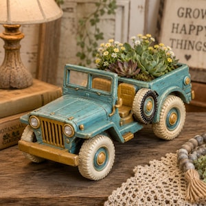 Könnte beinhalten: Türkisfarbener Jeep-Blumentopf mit Used-Look-Finish, gefüllt mit Sukkulenten und kleinen gelben Blüten. Der Jeep hat goldfarbene Akzente und cremefarbene Reifen, was eine rustikale, Vintage-Ästhetik erzeugt. Ein einzigartiges Wohnaccessoire.