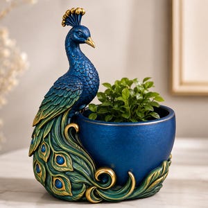May include: A decorative peacock-shaped planter featuring a deep blue and green finish with gold accents. The peacock stands beside a rounded, bowl-shaped container that holds a small green plant, with detailed feather textures and eye patterns.