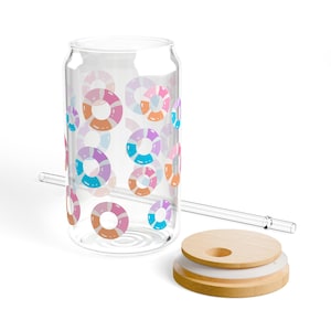 Puede incluir: Un vaso transparente en forma de lata con un colorido diseño de salvavidas. El vaso tiene una pajita transparente y una tapa de madera. Los salvavidas son de color rosa, naranja, morado y azul.