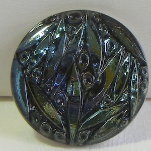 May include: A round, iridescent button with a dark, multi-colored finish. The button features a pattern of leaf-like shapes and small, circular accents. The button's surface reflects shades of blue, green, and gold.
