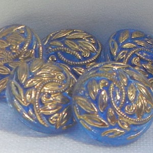 May include: Five round blue buttons with gold leaf-like designs. The buttons have a slightly domed shape and a glossy finish. The gold detailing is raised, creating a textured appearance. These buttons are suitable for sewing and craft projects.