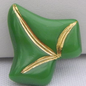 May include: A green, abstract-shaped button with gold-colored accents. The button has a glossy finish and a unique, asymmetrical design. The gold accents are in the shape of a leaf or feather.