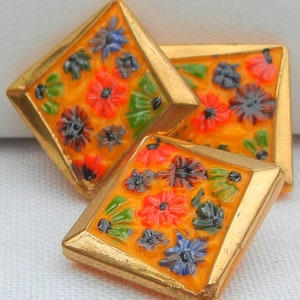 May include: Three diamond-shaped decorative buttons with a gold border and a vibrant orange background. Each button features a colorful floral design with red, blue, green, and gray flowers.