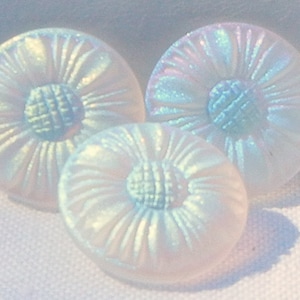 May include: Three iridescent white buttons with a textured, pleated design. Each button has a central, detailed, circular pattern. The buttons are arranged in a cluster, with varying sizes and subtle color shifts.