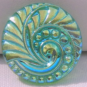 May include: Iridescent glass button with a swirling, spiral design. The button features a mix of teal, gold, and blue hues. The button has a textured surface with a series of small, raised circles and a detailed, fan-like pattern.
