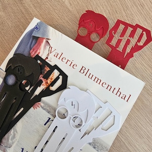 Op de afbeelding: Vier Harry Potter-thema bladwijzers in rood, zwart en wit. De bladwijzers tonen het silhouet van een personage met een bril, een bliksemschicht en het HP-logo. De bladwijzers liggen op een boek met de naam van de auteur, Valerie Blumenthal.