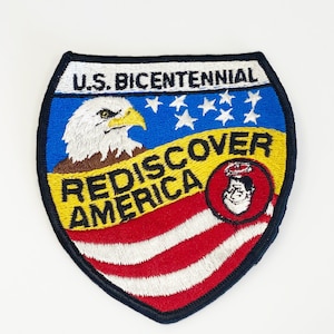 May include: An embroidered patch in red, white and blue featuring a bald eagle, stars and the text "U.S. BICENTENNIAL REDISCOVER AMERICA".