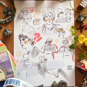 May include: A hand-drawn illustration featuring multiple sketches of a person wearing a chef's hat, with star accents on their face. The artwork includes the text "Locked in" and "DAN & PHIL 2018 WORLD TOUR". The drawing is surrounded by dice, a bracelet, and other small items.