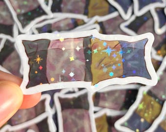 May include: A rectangular sticker with a white border. The sticker features a design with four vertical sections in shades of black, purple, yellow, and blue. Holographic stars are scattered across the design.