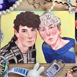 May include: An illustration of two people with light skin, one with brown hair and a plaid shirt, the other with white hair and a blue sweater. The artwork has a yellow background and is surrounded by jewelry and accessories.