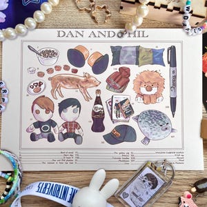 May include: A print titled "DAN AND PHIL" featuring illustrations of various objects, including a pig, dolls, a bottle of Ribena, and a Sharpie marker. The print is surrounded by beaded bracelets, a keychain, and other decorative items.