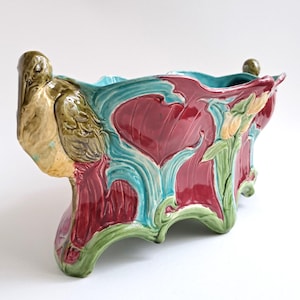 Può includere: Una fioriera in ceramica con un design Art Nouveau. La fioriera presenta una tavolozza di colori bordeaux, turchese e verde con motivi floreali e di uccelli scolpiti. La fioriera è lunga circa 30 cm, larga 15 cm e alta 20 cm.