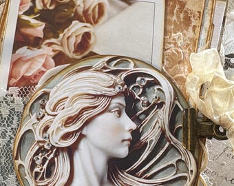 May include: A vintage-style journal with a cameo design featuring a woman's profile. The journal has aged paper pages, a floral print, and a decorative clasp. The color palette includes cream, beige, and touches of blue and gold.