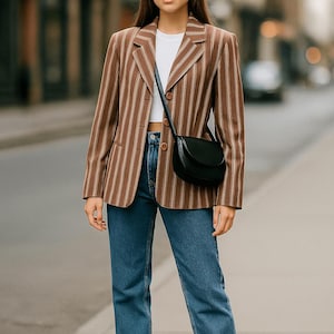 May include: A brown and white striped blazer, white top, and blue jeans. A black crossbody bag is worn over the shoulder. White trainers complete the outfit. The outfit is suitable for casual or business casual wear.
