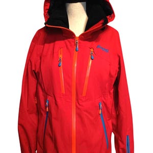 May include: Red ski jacket with a black fleece-lined hood, orange zipper, and blue accents. The jacket has multiple pockets with orange and blue zippers.
