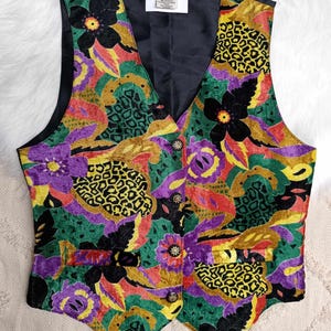 Puede incluir: Un chaleco colorido con un estampado floral y de leopardo. El chaleco tiene un forro de satén negro y está hecho de una tela suave y aterciopelada.