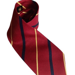 May include: A rolled red tie featuring vertical stripes in yellow and navy blue. The tie has a diamond pattern and a small label with gold detailing. This classic accessory is suitable for formal occasions.