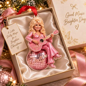 Può includere: Un ornamento decorativo con una figura bionda in un abito rosa scintillante che suona la chitarra, seduta su una palla da discoteca rosa con il nome Dolly. Include un'etichetta con la scritta A Little Dolly Magic for a Brighter Christmas e una scatola.