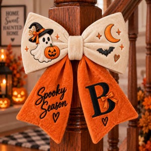 May include: A cream-coloured velvet bow featuring embroidered Halloween motifs including a ghost wearing a witch hat, a pumpkin, a crescent moon, and a bat. The orange velvet tails display the black text Spooky Season and a large letter B.