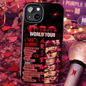 Puede incluir: Funda de teléfono negra con un diseño de BTS World Tour, con el texto "BTS IS BACK". La funda incluye títulos de canciones e imágenes de los miembros de la banda. Una rosa roja y una estrella acentúan el diseño. La funda está rodeada de corazones rojos.
