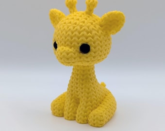 May include: A handmade yellow crochet giraffe with black eyes and small ears. The giraffe is sitting with its legs folded and has small horns on its head. The toy is made of a textured yarn.