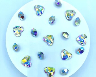 Op de afbeelding: Een verzameling iriserende strass-steentjes in hart- en ovale vormen op een wit, cirkelvormig oppervlak. De strass-steentjes schitteren in verschillende kleuren. Geschikt voor knutselen en versieringen. Afmetingen in centimeters.
