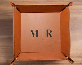 May include: A brown leather tray with a stitched border and a divider down the middle. The initials "M R" are embossed on the tray.