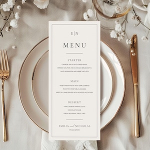 Peut inclure: Un menu de mariage rectangulaire avec une bordure noire et du texte. Le menu comprend des entrées, des plats principaux et des desserts. Les noms "Emilia" et "Nicholas" sont en bas, avec la date 05.22.2026. Des couverts dorés et des assiettes blanches sont également visibles.