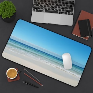 May include: A blue and white beach scene with white sand and blue water. The image is on a black mouse pad with a white computer mouse on the pad.