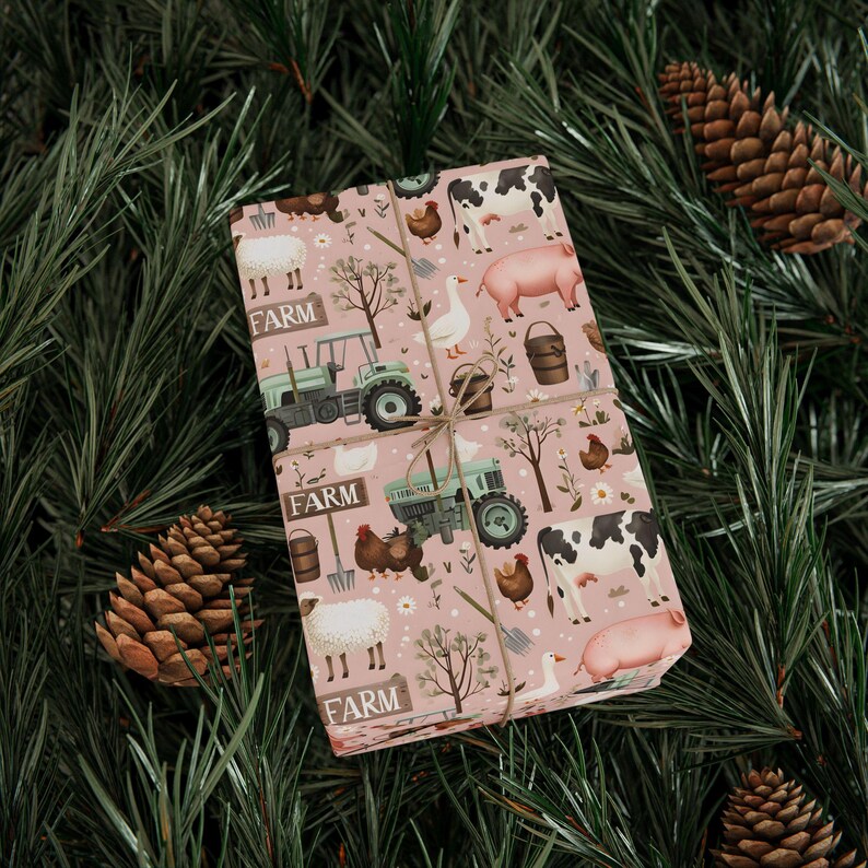 May include: A wrapped gift featuring farm-themed wrapping paper. The paper has a pink background with illustrations of farm animals, tractors, and the word "FARM". The gift is tied with twine and set against a backdrop of pine needles and pine cones.