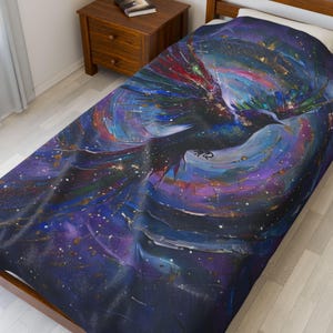 May include: A dark blue throw blanket with a colorful abstract design of a bird flying through a galaxy. The design features shades of purple, blue, green, red, and gold.
